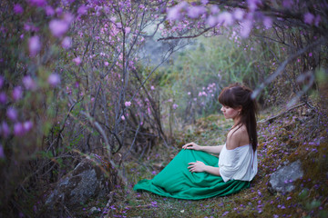 A girl walks in bloom of flowers against the backdrop of a mountain landscape.