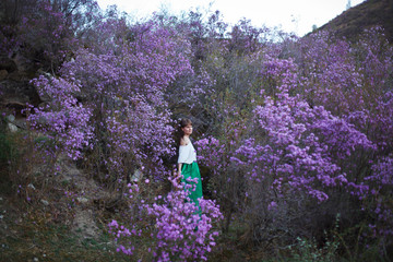 A girl walks in bloom of flowers against the backdrop of a mountain landscape.