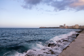 Scenic view of waves crashing on the Malecon seawall at dusk, with the Morro Castle and the old town in the background, Havana, Cuba