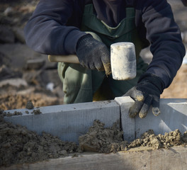 A worker knocks a hammer on a concrete curb, close-up.