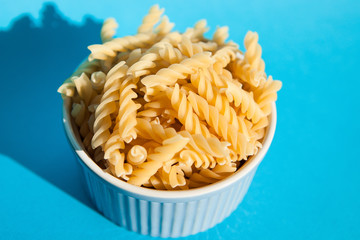 Rotini pasta in bowl on blue background