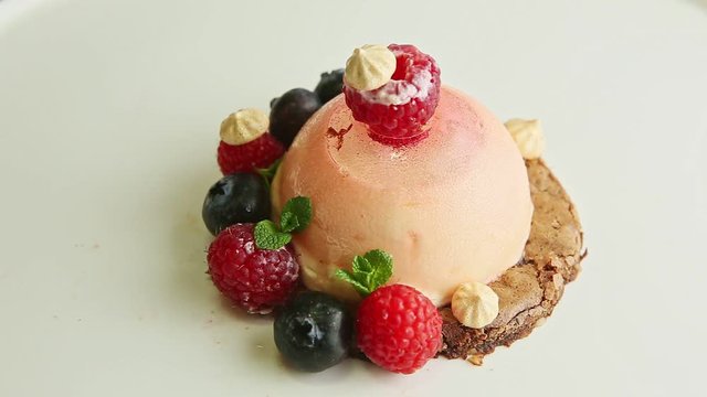 top view closeup pink icing dessert trendy decorated with fresh mint, raspberries, blueberries, and bize rotates on modern restaurant plate