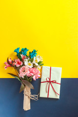 A colorful spring flowers bouquet with a present box on the multicolored paper background. Possible concepts of birthday, valentines day, anniversary, mothers day, wedding, love