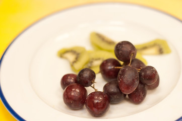 Top view, close up of washed red grapes and slicedkimi as food pairings, on a round, white plate, for a tropical wine tasting event