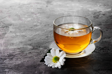 Herbal tea with camomile on a dark background. A cup of tea with herbs and dried apples on a gray concrete table. Vitamin drink.