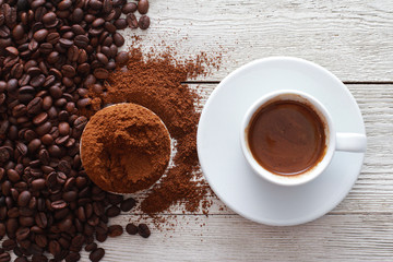 White cup of coffee with foam, roasted and ground beans on wooden table. Closeup, copy space, top view. Coffee shop, espresso, fresh roast, drink  concept