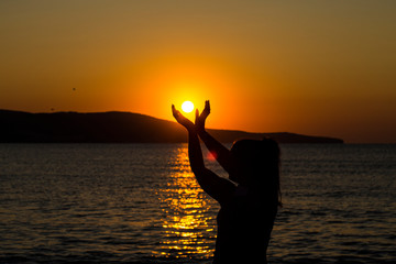 The girl holds the sun in her hands. Beautiful sunrise on the sea.