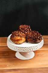 Top, front view, close distance of three, freshly baked, homemade  pecan stickey buns, on a white, round, pedestal, ceramic display dish 