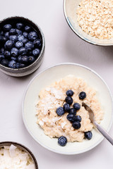 Oats porridge with blueberries and coconut crunchies on light concrete background. Healthy diet breakfast. Flat Lay. Selective focus