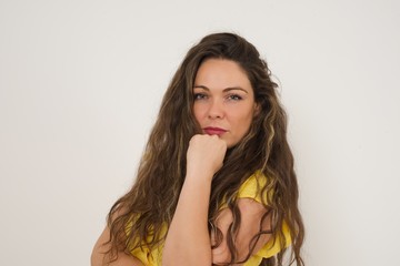 Isolated portrait of stylish young European woman with hand under chin and looking sideways with doubtful and skeptical expression, suspect and doubt. Standing indoors over background.