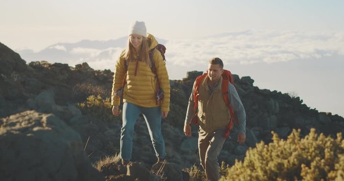Young active couple hiking up a mountain above the clouds with backpacks, adventurous backpackers in the great outdoors