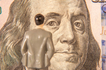 Male miniature figure studying a US 100 dollar bill