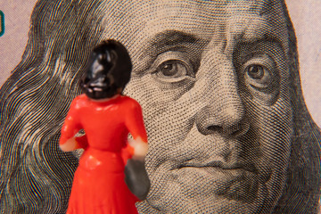 Female miniature figure studying a US 100 dollar bill