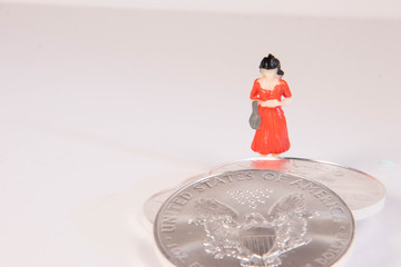 A female miniature figure standing behind US silver eagle coins