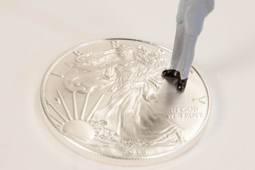 A male miniature figure standing on a US silver eagle one once coin