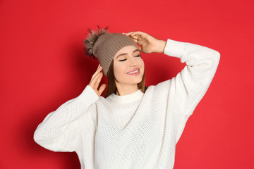 Young woman wearing warm sweater and hat on red background. Winter season