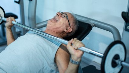 Fototapeta na wymiar Uomo anziano fa degli esercizi con i pesi in palestra