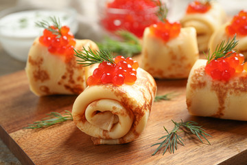 Delicious thin pancakes with red caviar on wooden board, closeup