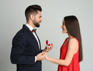 Man with engagement ring making marriage proposal to girlfriend on light grey background