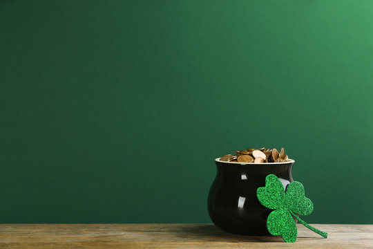 Pot of gold coins and clover on wooden table against green background, space for text. St. Patrick's Day celebration