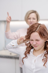 Fototapeta premium The teenage girl closed her eyes and closed her ears. Her mother in the background chastises her. Relationship problems, puberty