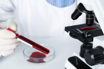 Scientist holding test tube with blood sample at table, closeup. Virus research
