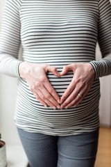 Fototapeta premium pregnant woman with hands shaping heart on her belly