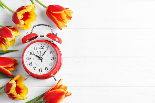 Red alarm clock, spring flowers and space for text on white wooden table, flat lay. Time change