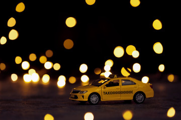 Yellow taxi car model on table against festive lights. Bokeh effect