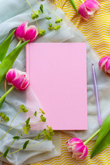 pink diary in a fabric cover lies among women's clothing in delicate shades and flowers of tulips, flat lay