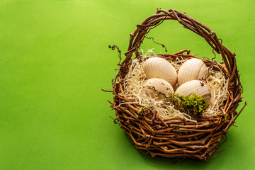 Easter wicker basket. Zero waste, DIY concept. Wooden eggs, shavings, moss. Green bright background