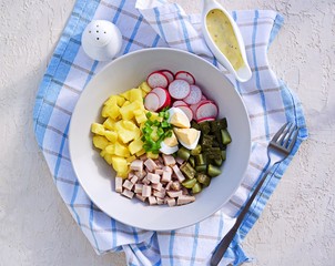Potato salad with ham, fresh radish and pickled cucumber in a gray bowl on a light concrete background. American cuisine. Potato Recipes. Top view