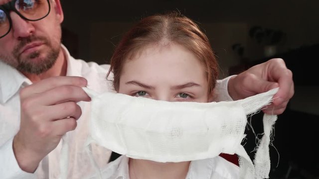White man in white shirt ties medical face mask to face of white calm girl. BCU