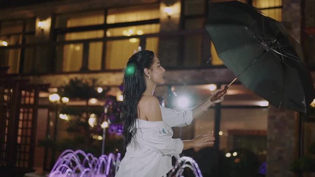 Happy brunette with long hair twists an umbrella and smiles in night city