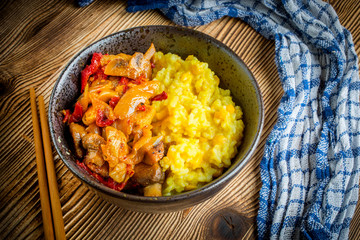 Saffron rice with pieces of chicken and vegetables on wooden table.