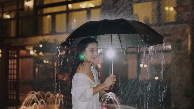 Seductive model plays with umbrella at fountain in night city
