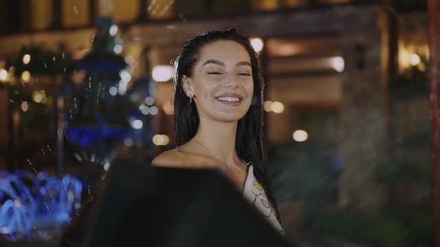 Pretty wet woman twisting an umbrella at camera under the night rain