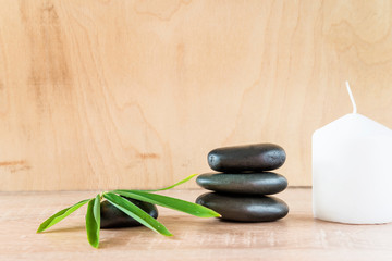 Pyramid of black massage stones, bamboo leaves and white candle on wooden background. Space for text