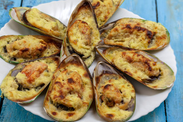 Oven baked mussels in creamy garlic sauce with lemon in a plate on a blue background