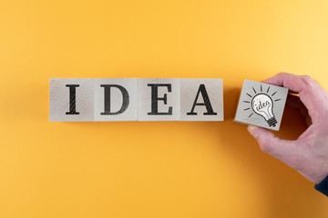 top view of wooden toy blocks with word IDEA and light bulb icon against orange background,...