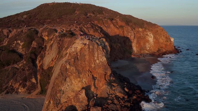Tourists on Point Dume cliffs at sunset, panning aerial