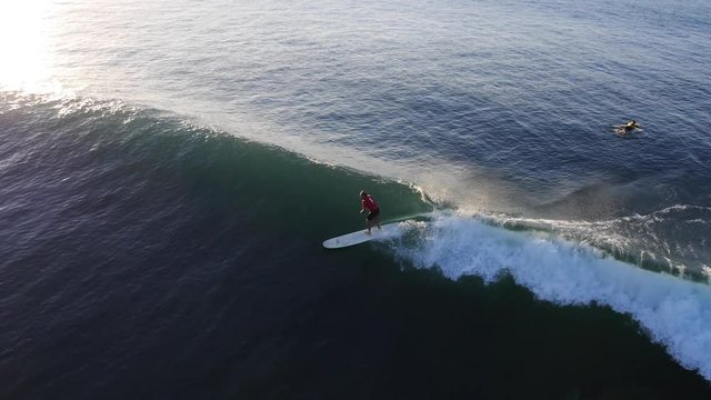 Pan left aerial, surfer catches wave at sunset in Malibu