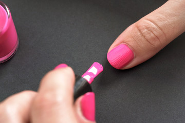 Applying pink nail polish - closeup photo of woman fingernail and little brush with paint on gray black background