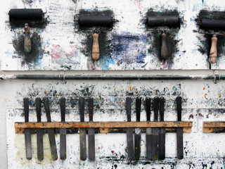 Printmaking rollers hanging on an art studio wall in the messy workshop