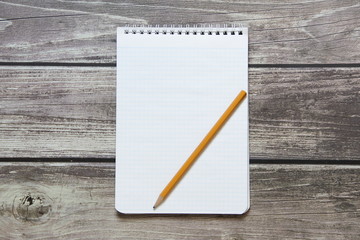 Notepad with a blank white sheet in a checker paper with simple graphite pencil lies on the background of wooden boards.