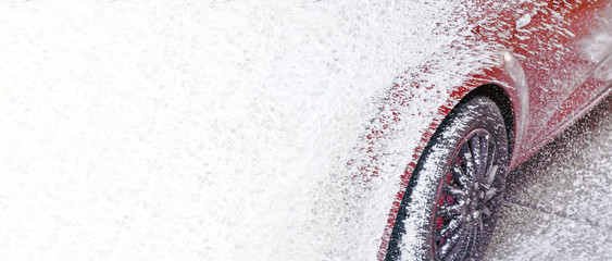 Red car washed in self serve carwash, detail on white soap sprayed onto surface transition to...