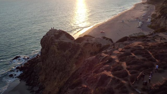Tourists on Point Dume cliffs in Malibu at sunset, pan left aerial