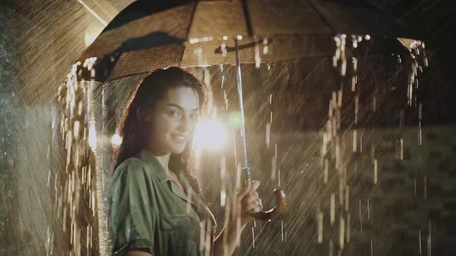 Portrait of admiring girl stands with umbrella under night heavy rain