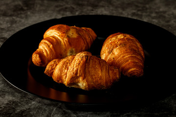 Freshly baked French croissants with cappuccino milk on a dark background with copy space.
