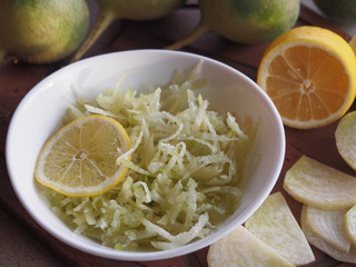 Salad of raw grated green radish and lemon in a white bowl, vegetables, pieces of radish on a wooden stand closeup. Recipe for a vegetarian dish for proper nutrition.